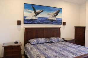 A bedroom with a bed, nightstands, a wooden headboard, a wall-mounted painting of whales, and a dresser. - Misiones del Cabo 4206. 1BR Completely Remodeled Ocean View Condo! (Cabo San Lucas)