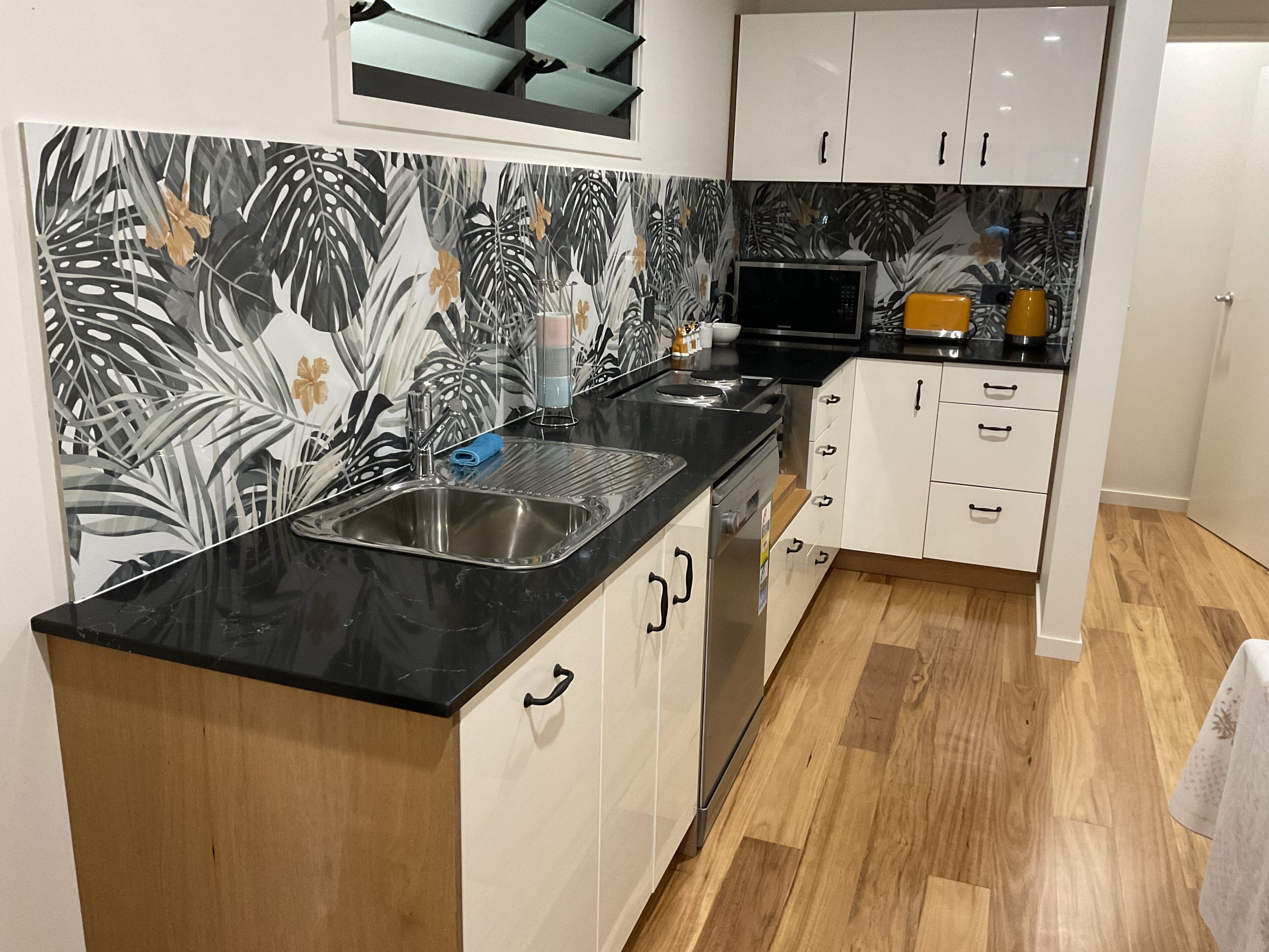 A modern kitchen with a black countertop, white cabinets, and a tropical leaf-patterned backsplash.