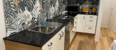 Une cuisine moderne avec un plan de travail noir, des armoires blanches et un pare-feu décoré de motifs de feuilles tropicales.