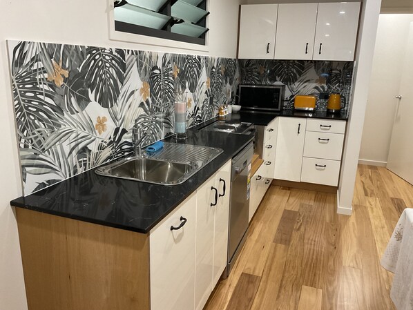 A modern kitchen with a black countertop, white cabinets, and a tropical leaf-patterned backsplash.