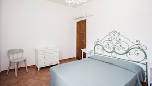 Een slaapkamer met een bed, een stoel, een dressoir en een deur.