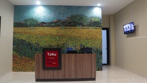 A reception desk with a sign reading "Toku House di Slipi" and a large painting of a field with trees and a tower in the background. - Djuragan Kamar Slipi (Jakarta)