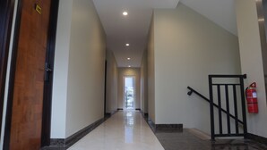 A hallway with a wooden door labeled "102", a fire extinguisher mounted on the wall, and a black metal railing. - Djuragan Kamar Slipi (Jakarta)