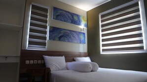 A hotel room with a bed, two paintings on the wall, and two windows with blinds. - Djuragan Kamar Slipi (Jakarta)