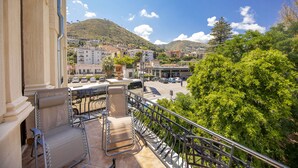 Un balcon doté d’une rambarde en métal, donnant sur un parking et des immeubles, avec une vue sur une colline et des arbres en arrière-plan.