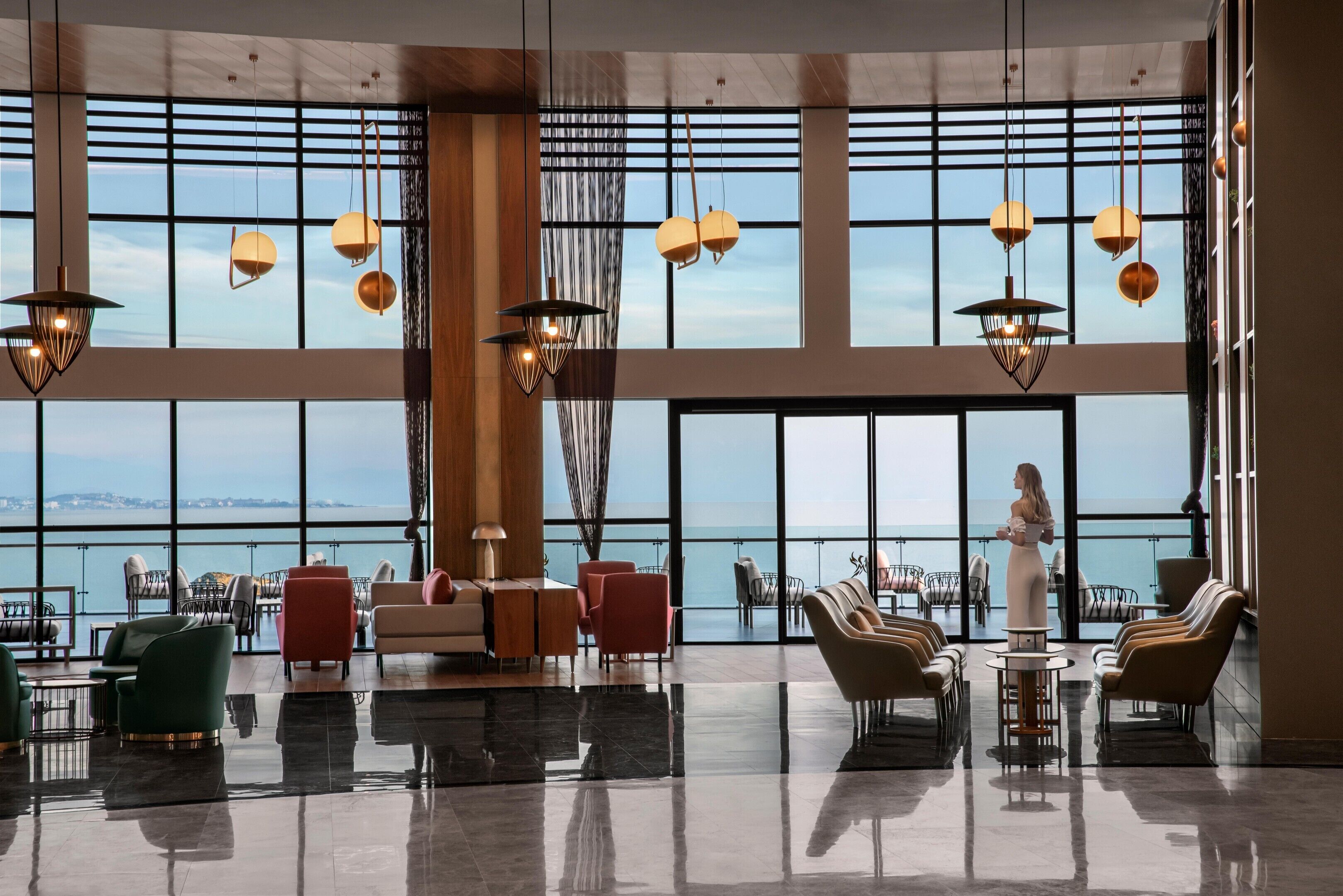 A spacious lobby with large windows, multiple seating areas, and hanging pendant lights.