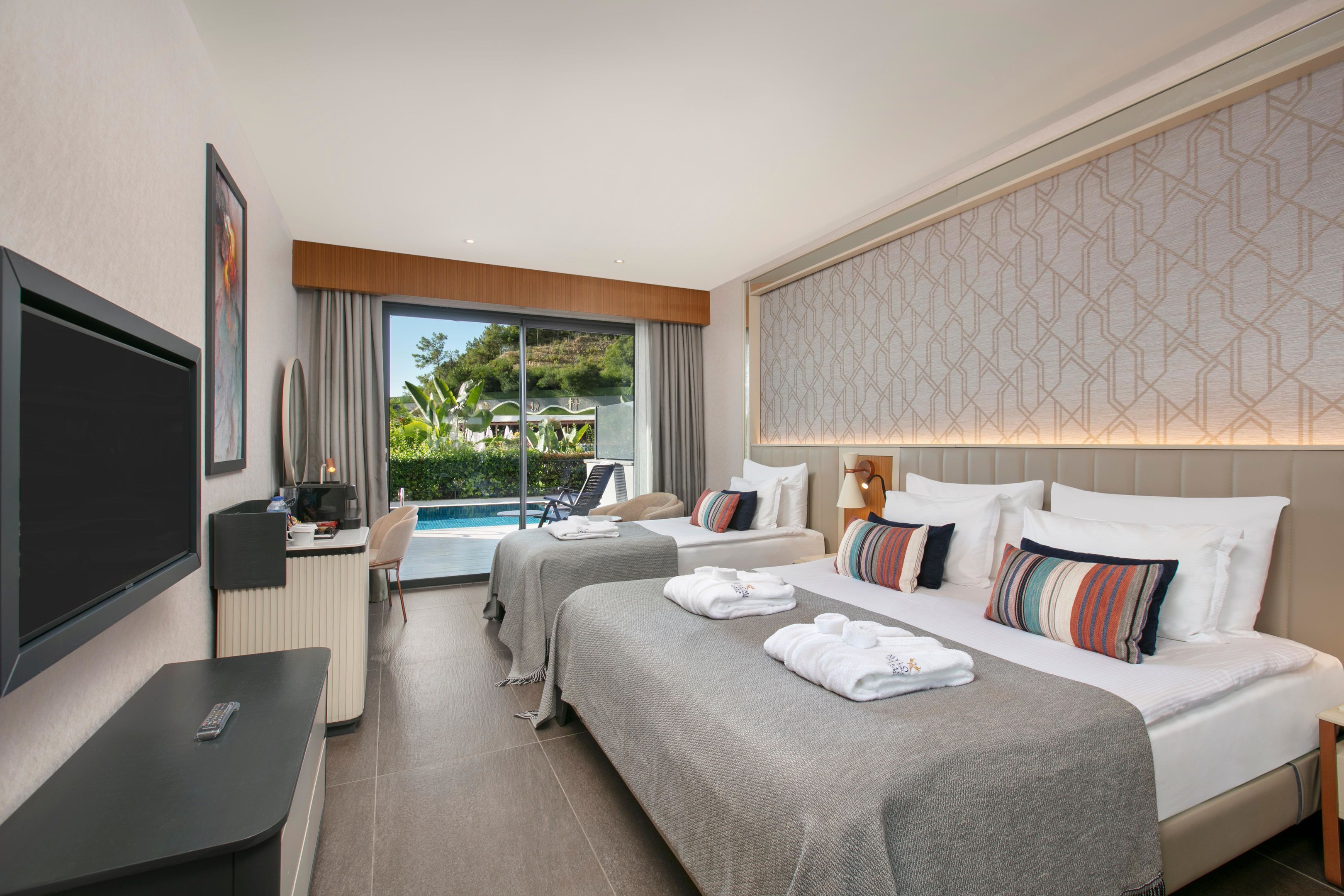 A hotel room with a TV, a desk, two beds, a pool view, and a patterned wall.