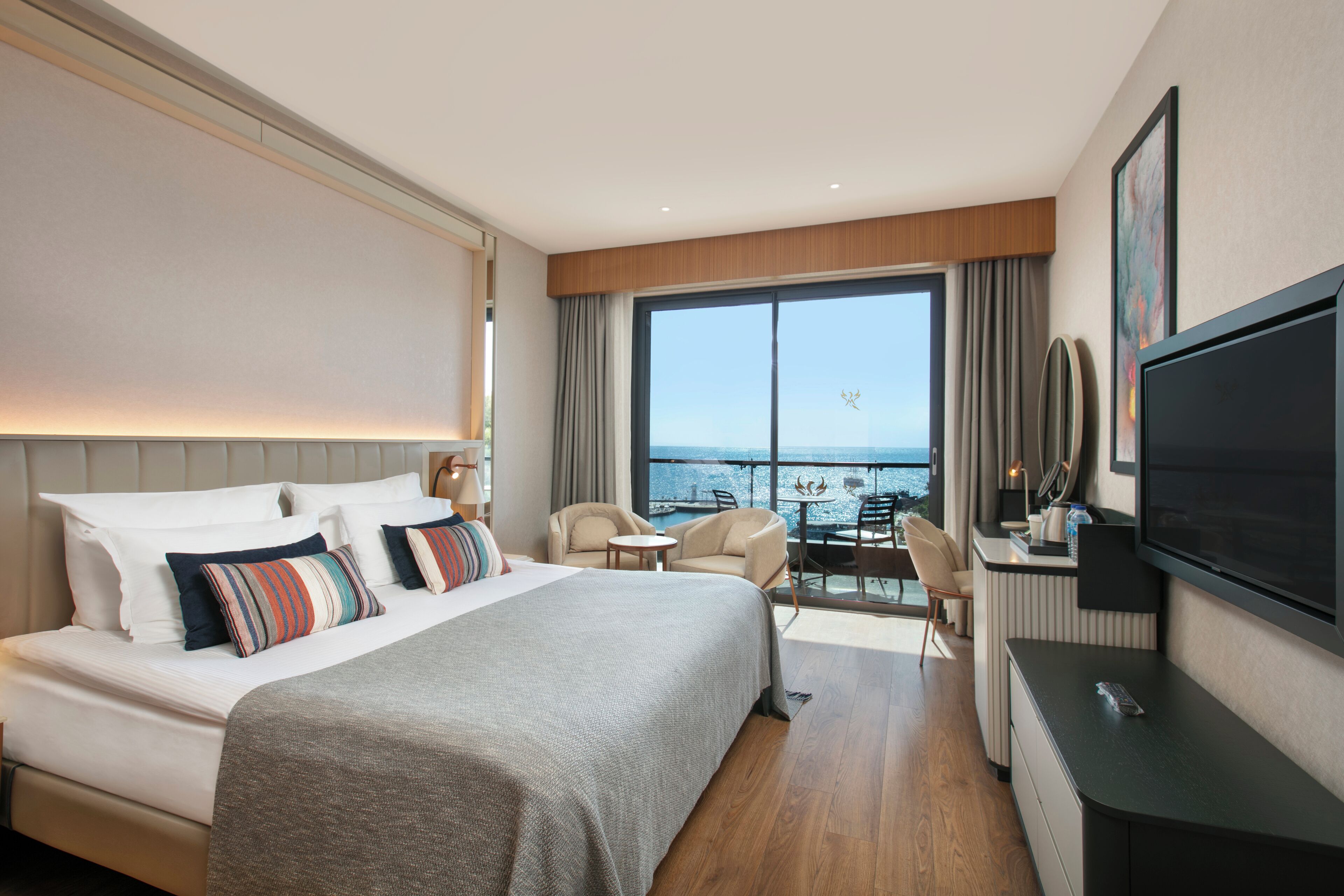 Una habitación de hotel moderna con una cama grande, un escritorio, un televisor y un balcón con vistas al mar.