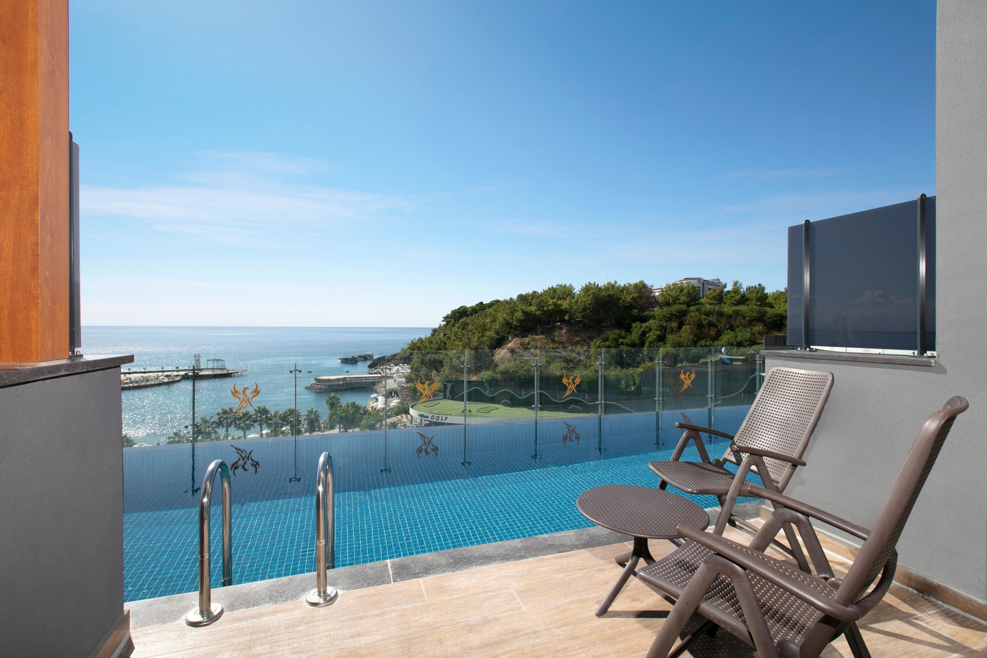 A balcony with a pool, lounge chairs, and a view of the sea.