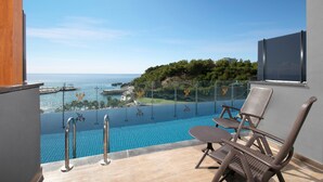 Un balcón con piscina, sillas de descanso y vista al mar.