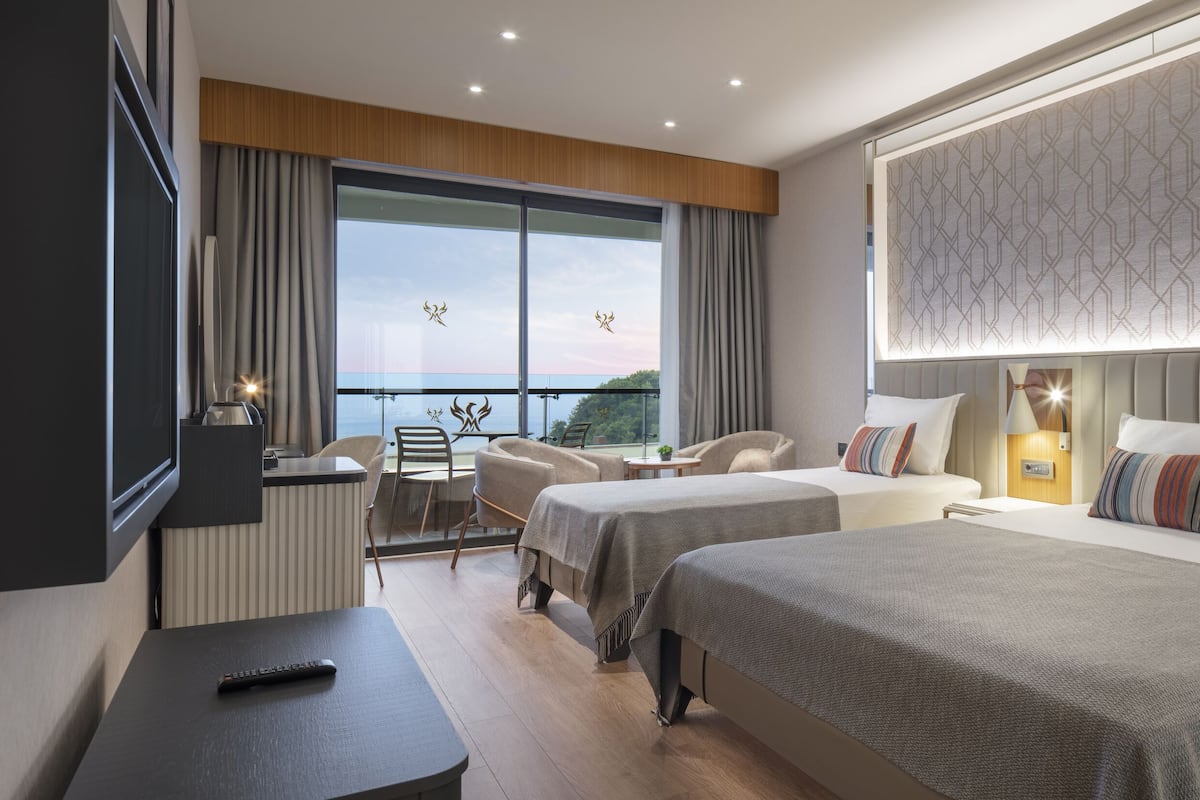 Ein Hotelzimmer mit zwei Betten, einem Fernseher, einem Schreibtisch und Meerblick.