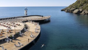 Eine Steg mit Liegestühlen und Sonnenschirmen, ein Leuchtturm und klares, blaues Wasser.
