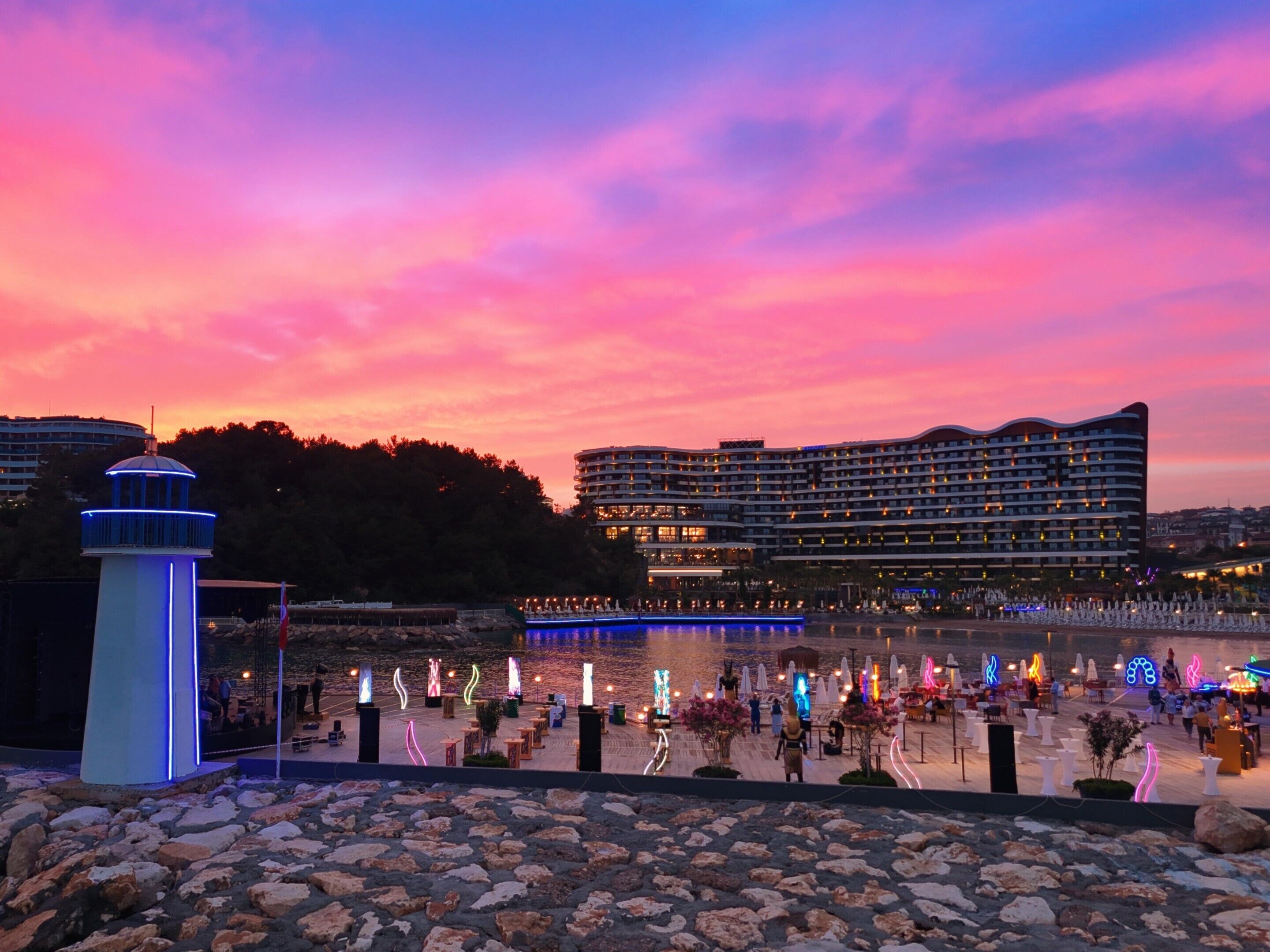 A waterfront hotel with a large building, a dock, and a rocky foreground.