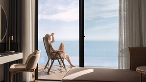 Ein modernes Zimmer mit einer großen Schiebeglasdoor zur Balkon mit Meerblick. Zwei Stühle und ein kleiner Tisch befinden sich auf dem Balkon.