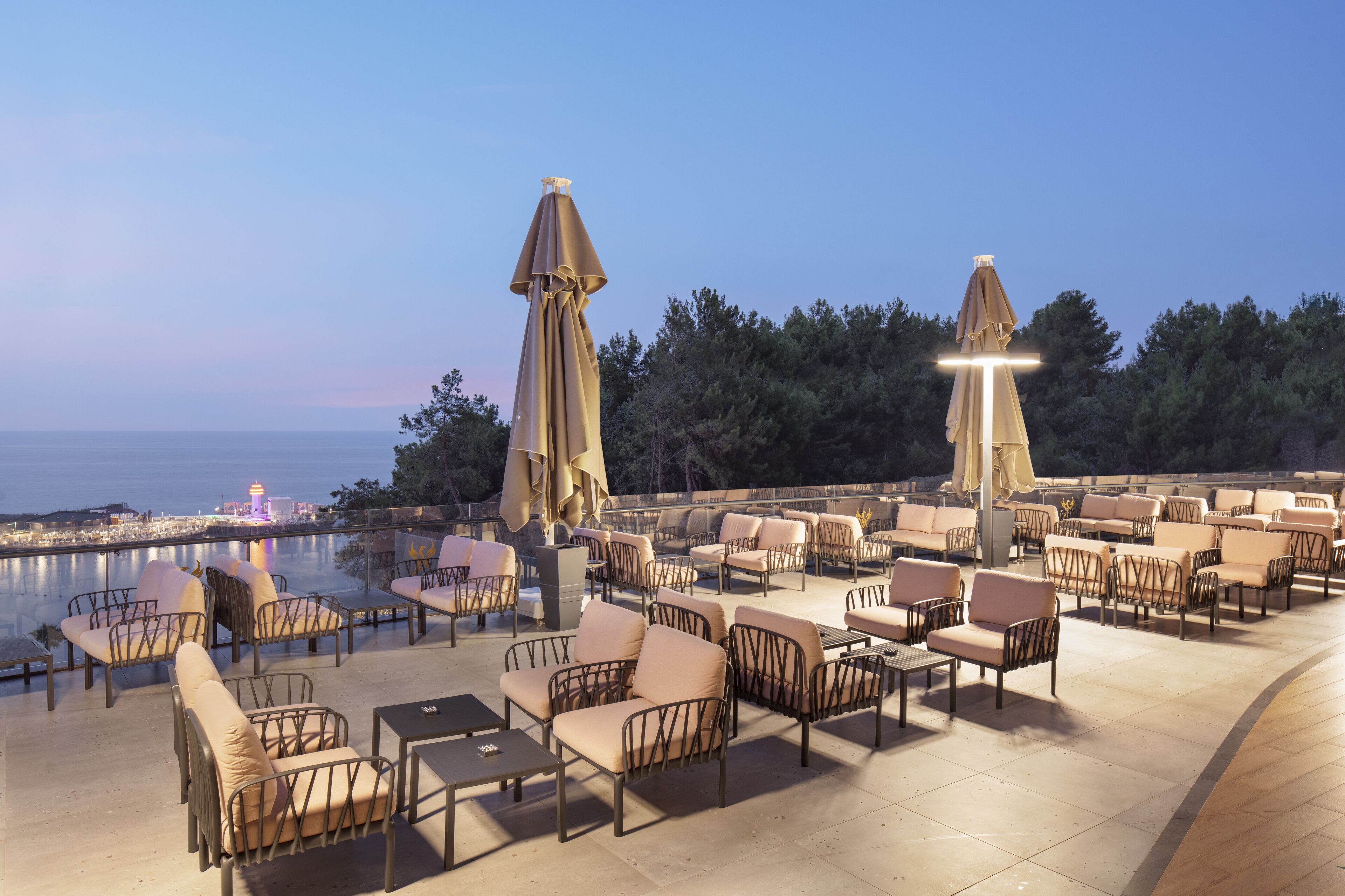 An outdoor seating area with multiple chairs and tables, umbrellas, and a view of the sea.