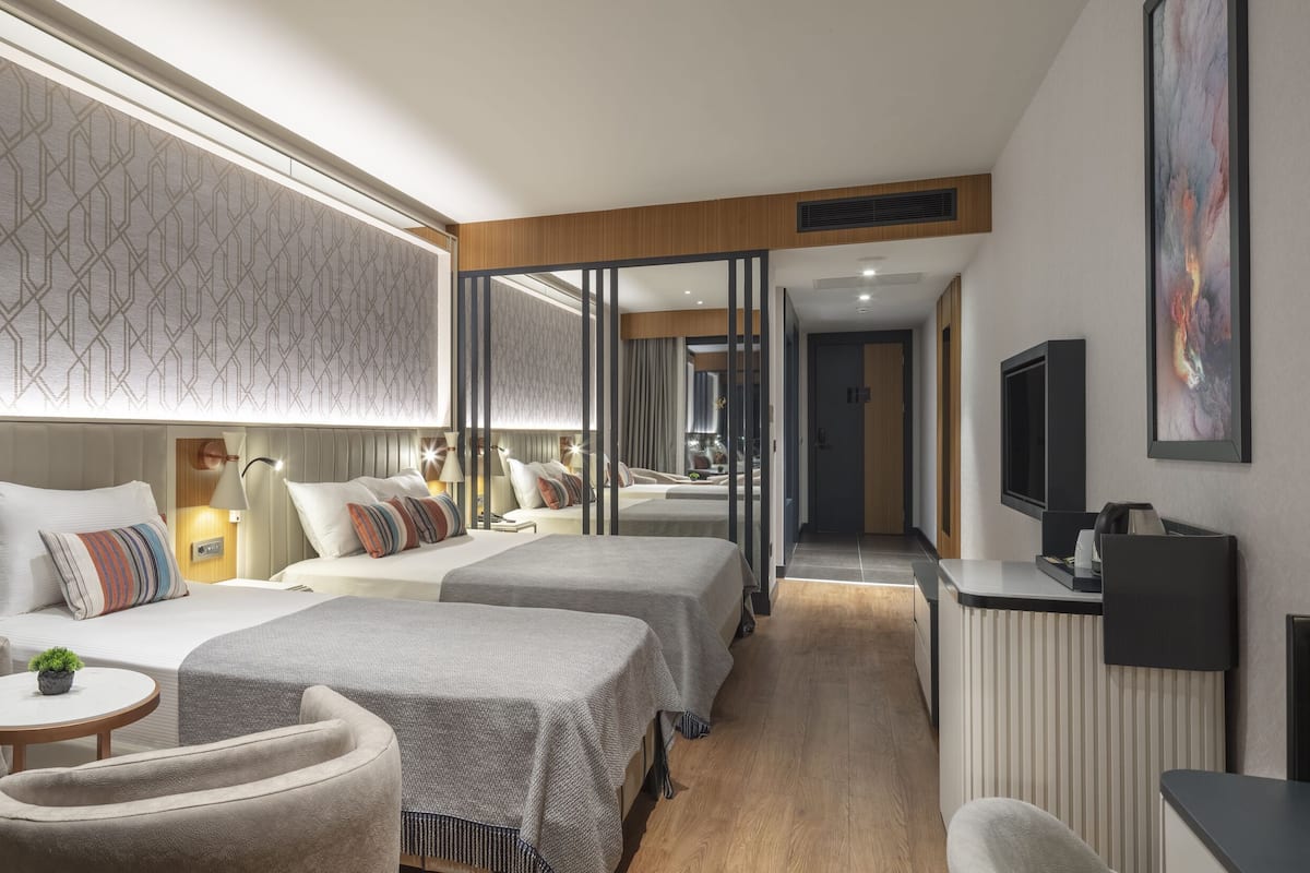 Ein modernes Hotelzimmer mit einem Bett, zwei Nachttischen, einem Schreibtisch, einem Sessel und einem Fernseher.