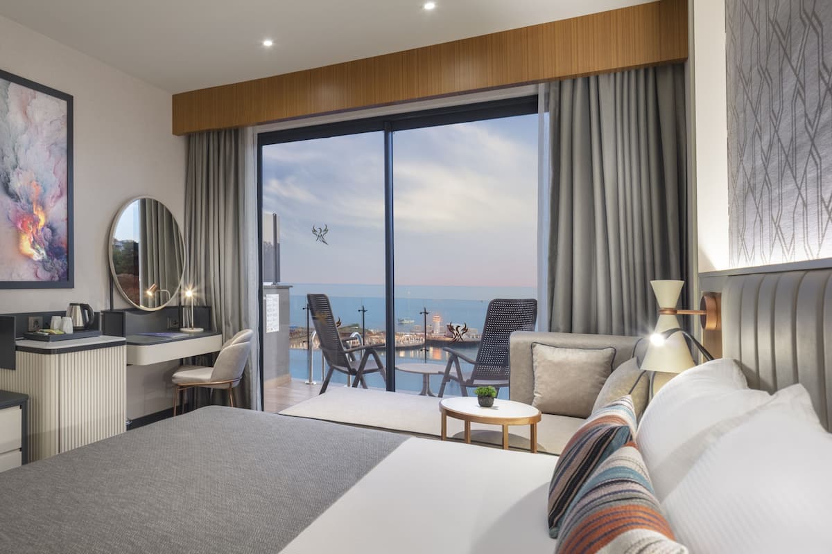 Ein modernes Hotelzimmer mit einem großen Bett, einem Schreibtisch, einem Fernseher, einem Balkon mit Stadtblick und einem großen Fenster.
