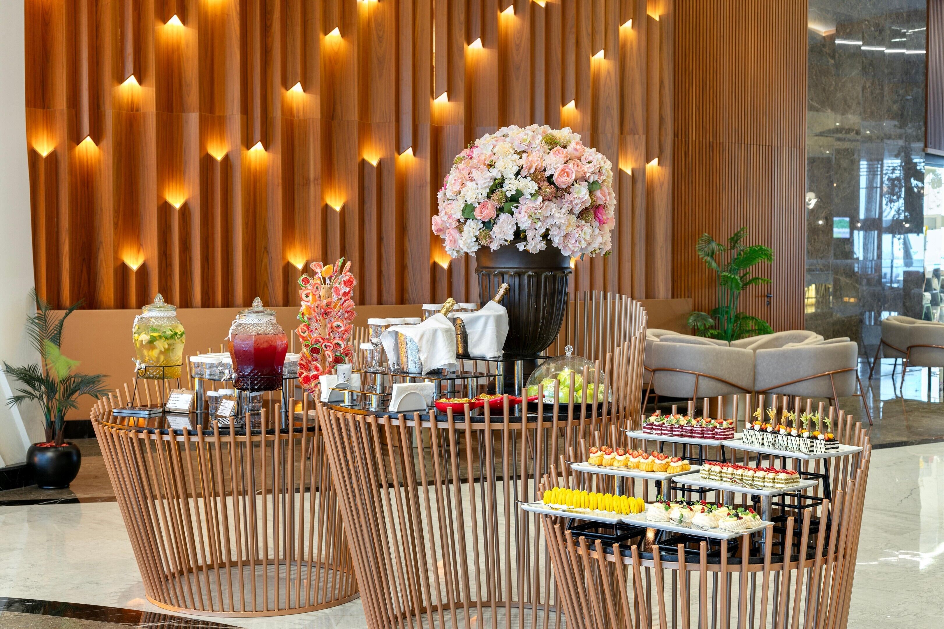 Disposição de buffet com diversos alimentos, um arranjo floral e decoração moderna com painéis de madeira e iluminação suave.