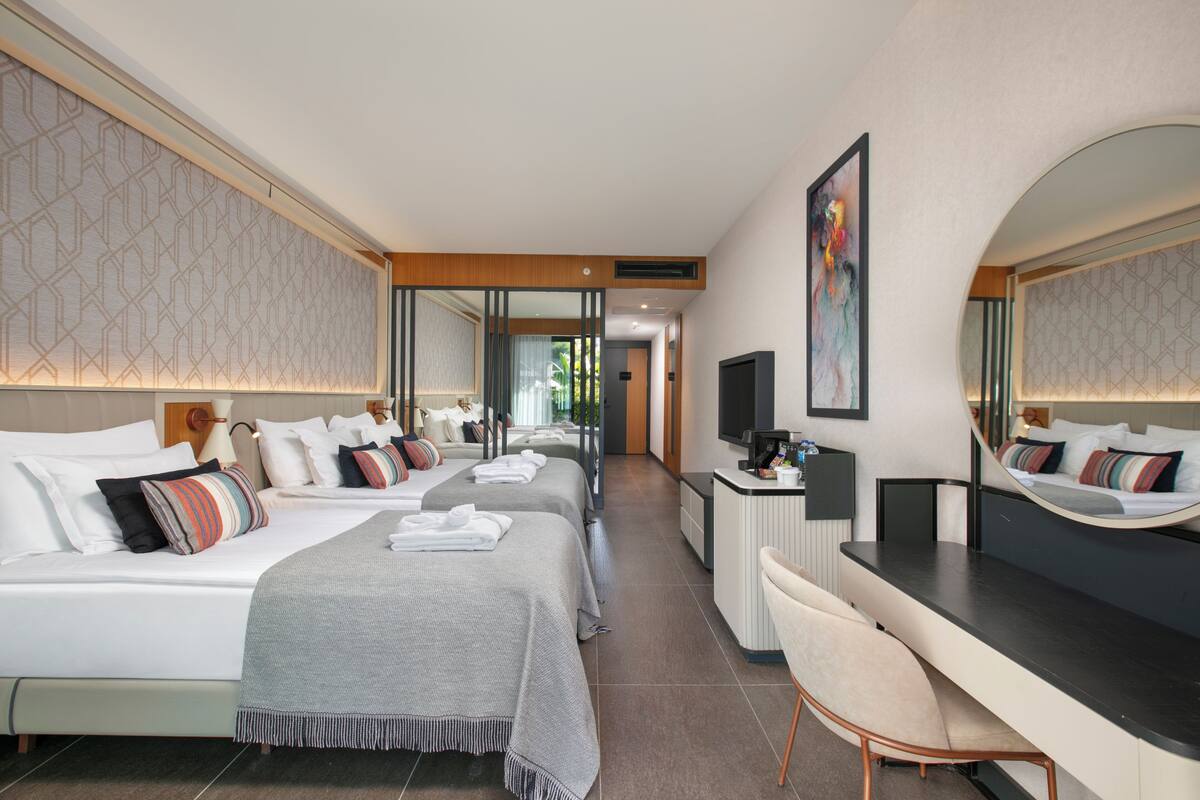 Ein Hotelzimmer mit zwei Betten, einem Schreibtisch, einem Stuhl, einem Fernseher und einem großen Spiegel.