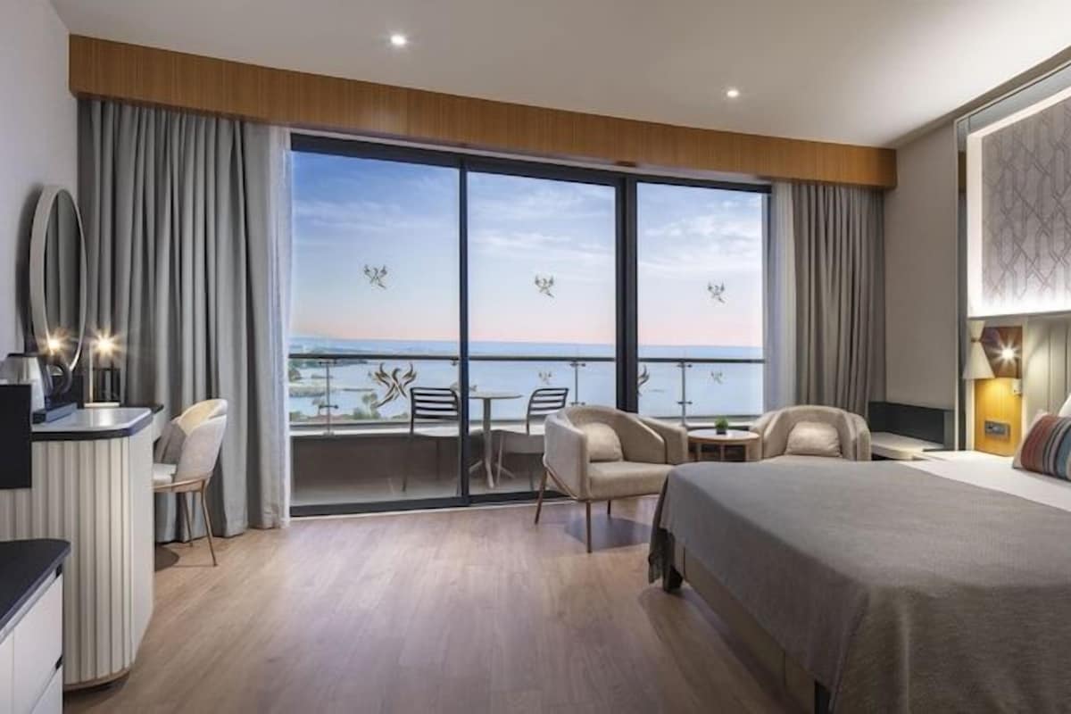 A modern hotel room with a large bed, a balcony with a view, a desk, and a chair.
