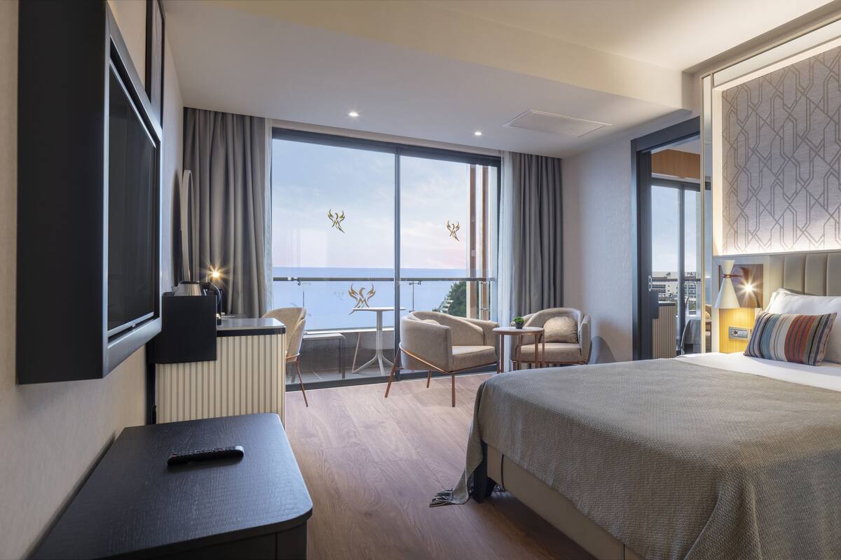 Ein modernes Hotelzimmer mit einem großen Bett, einem Schreibtisch, einem Stuhl und einem Balkon mit Blick.