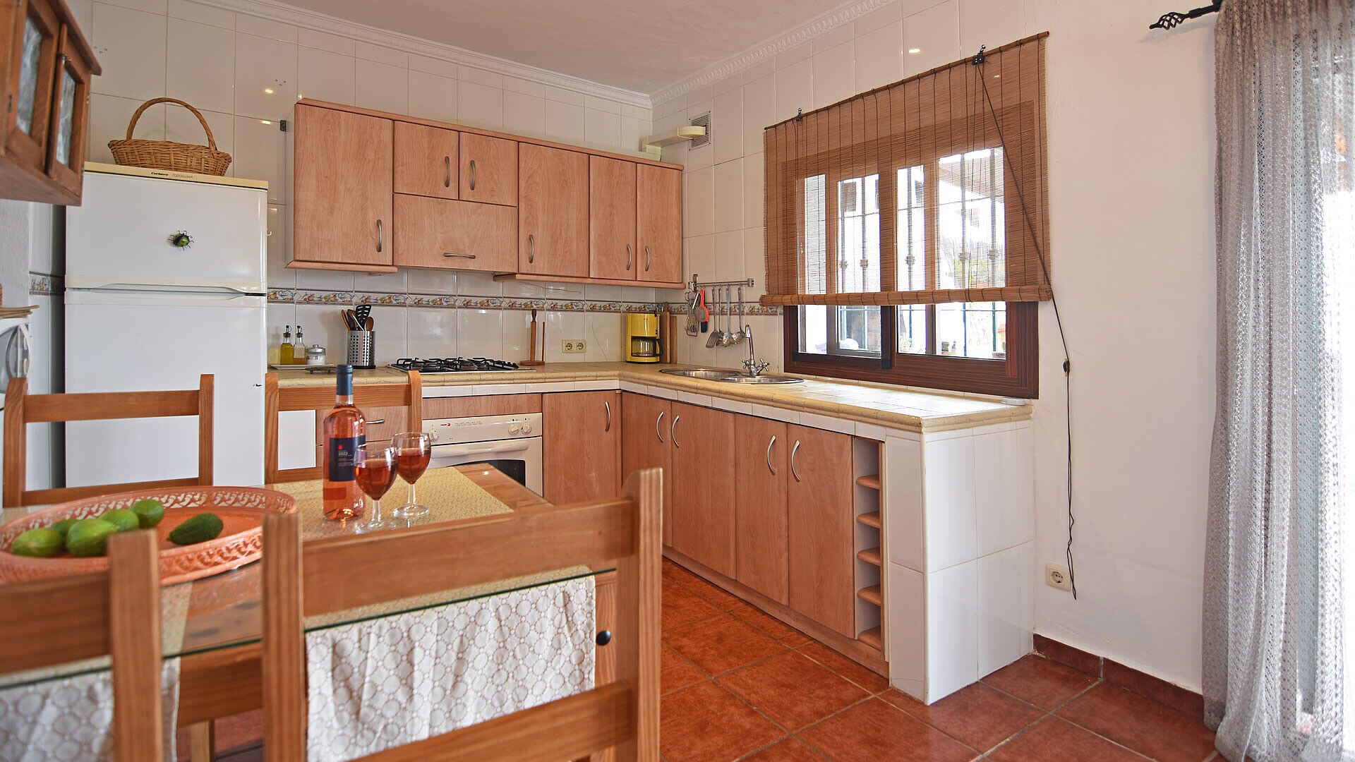 A compact kitchen with wooden cabinets, a dining table with chairs, and a window with blinds.