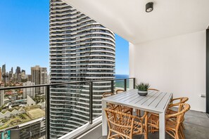 A balcony with a white table and wicker chairs, overlooking a cityscape and a tall building. - Koko Broadbeach (Broadbeach)