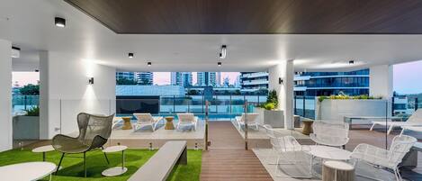 A rooftop lounge with a wooden deck, white lounge chairs, and a small pool area.