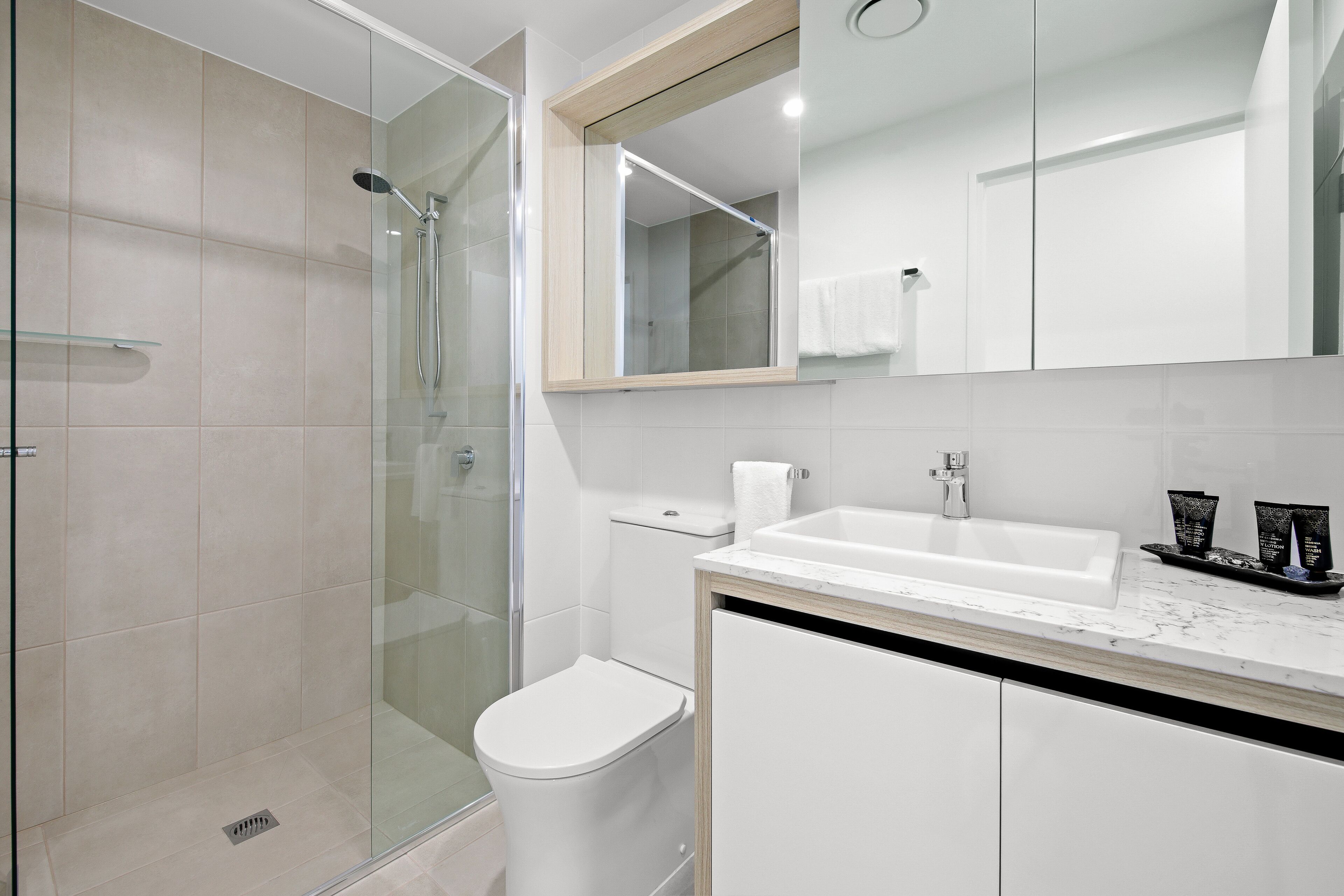 Une salle de bain moderne avec une douche à parois de verre, des toilettes blanches et un lavabo doté d’un plan de travail en marbre.