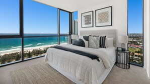 A bedroom with a large bed, a nightstand, and a view of the ocean. - Koko Broadbeach (Broadbeach)