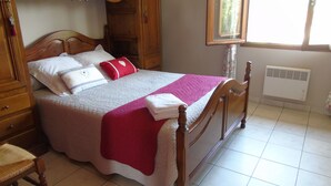 Een net opgemaakt bed met een houten hoofdbord, een rood kussen en een witte, opgevouwen handdoek.