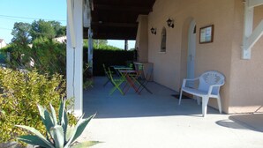 Een terras buiten met een witte plastic stoel, een tafel en meerdere opklapbare stoelen.