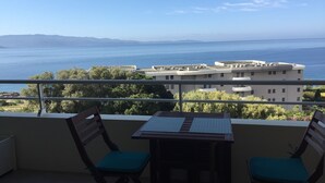 Un balcón con una mesa y dos sillas, con vistas al mar y edificios.