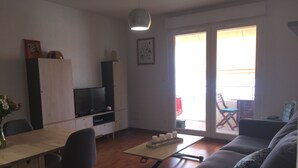 Una sala moderna con un sofá, un televisor sobre un mueble bajo, una mesa de comedor con sillas y una puerta corrediza de vidrio que da a un espacio exterior.