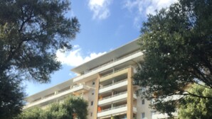 Un edificio de varios pisos con balcones, rodeado de árboles y follaje.