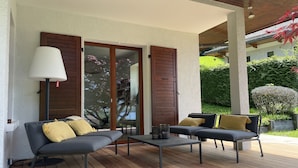A covered patio with two sofas, a table, and a floor lamp. - Villa (Talloires-Montmin)