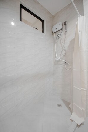 Un baño con paredes de azulejos blancos, una ducha con cabezal de ducha manual y una cortina blanca.
