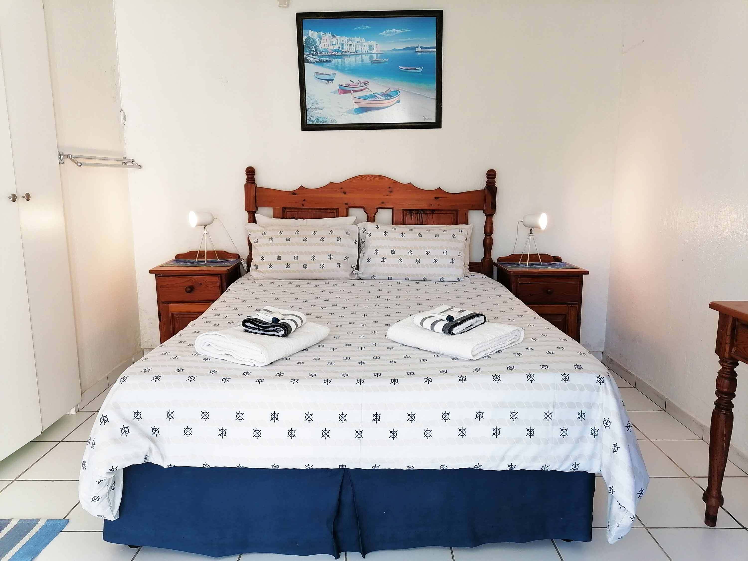 A neatly made bed with a patterned bedspread, two pillows, and two folded towels on the bed.