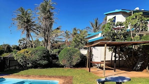 Un patio trasero con piscina, un porche techado y una casa con techo azul.