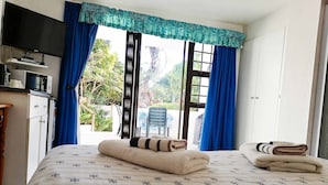 Habitación de hotel con cama, televisión, kitchenette pequeño y vista al exterior.