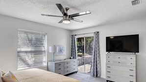 Un dormitorio con cama, cómoda, televisor y ventilador de techo.