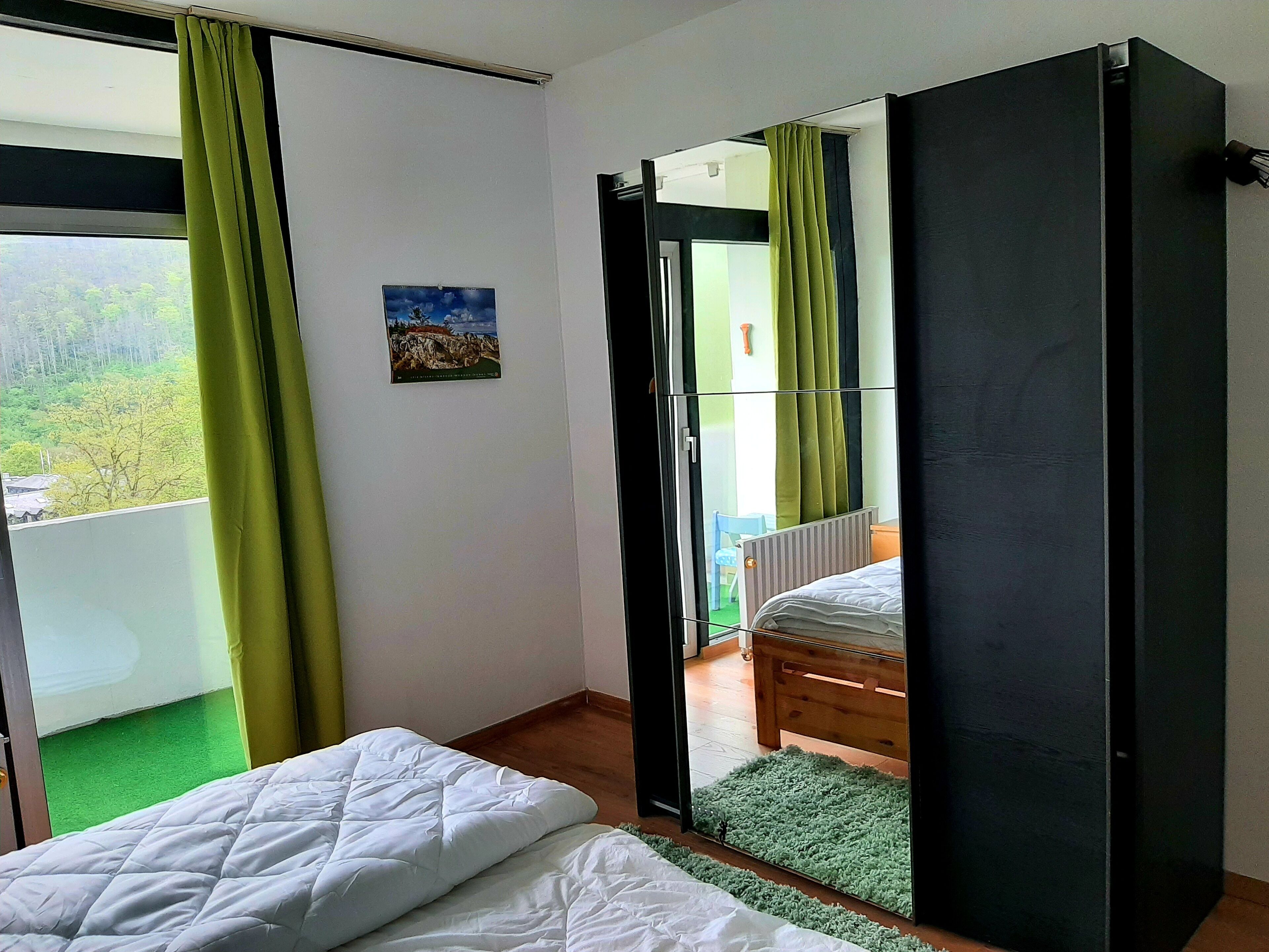 Une chambre à coucher avec un lit, un tapis vert, un tableau et une vue sur un balcon avec des rideaux.