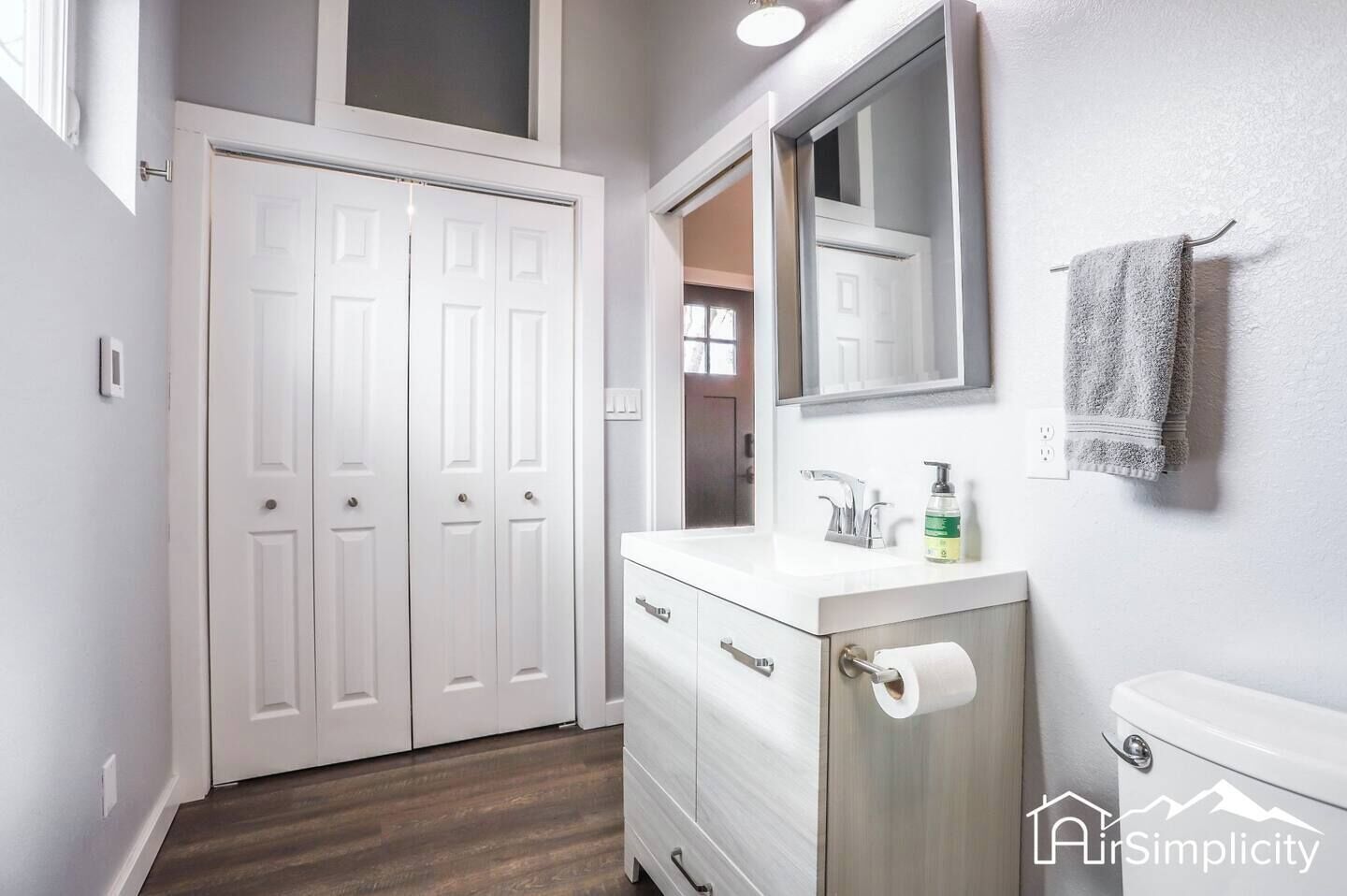 A bathroom with a white vanity, a mirror, a toilet, and a towel hanging on the wall.