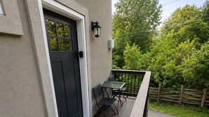 Eine Holzdielen-Terrasse mit Tisch und Stühlen, einer schwarzen Tür und einer Lampe.