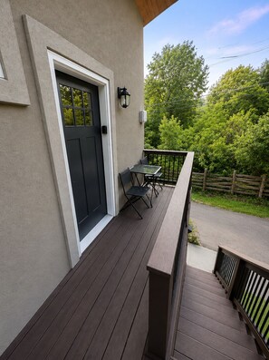 A wooden deck with a table and chairs, a black door, and a light fixture.