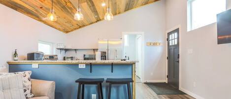 A modern kitchen with a wooden ceiling, bar stools, and a built-in island.