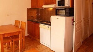 A compact kitchen with wooden cabinets, a microwave, a built-in oven, a dishwasher, and a dining area with a wooden table and chairs.
