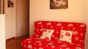 A room with a red sofa bed with heart and house patterns, a door, and a framed picture on the wall.