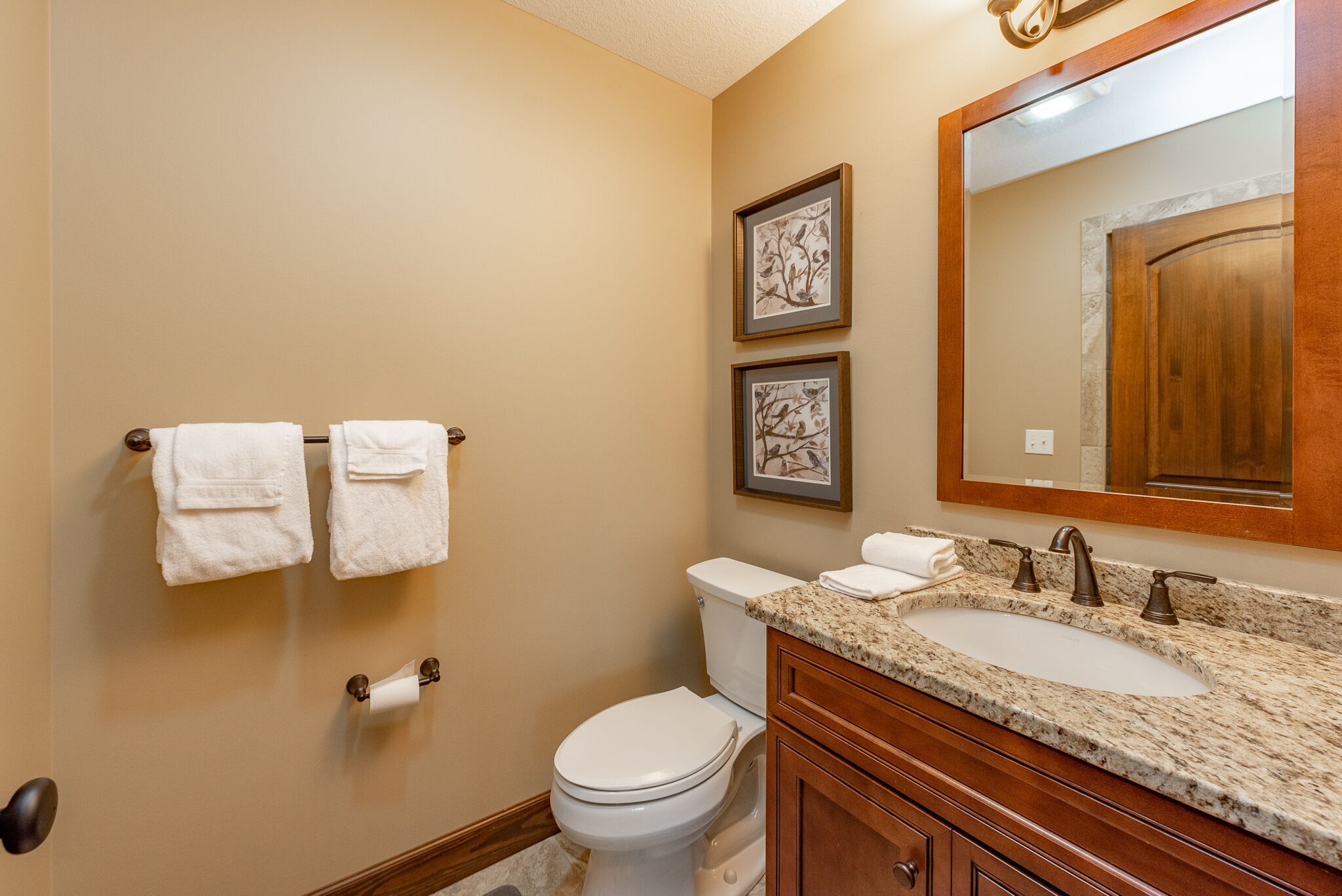A bathroom with a toilet, sink, and two framed pictures on the wall.