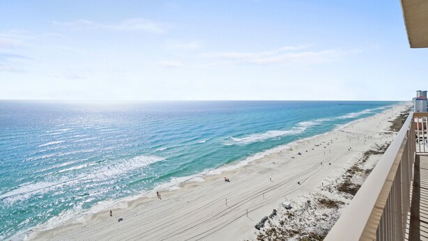 A beach view from a balcony with a clear sky, a sandy beach, and a pier in the distance. - Sunrise Beach 1611 Gulf Front Corner Condo Sleeps 10 (Panama City Beach)